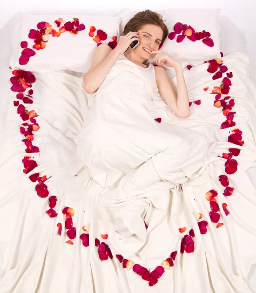 Kvinna ljuger i sängen omfattas av blomblad — Stockfoto