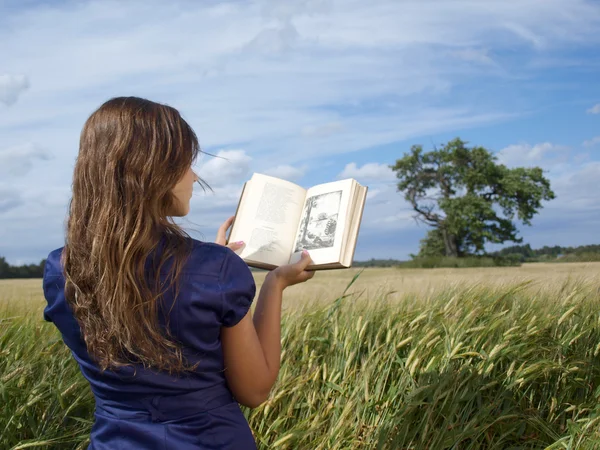 Junges Mädchen liest auf Gras bei blauem Himmel — Stockfoto