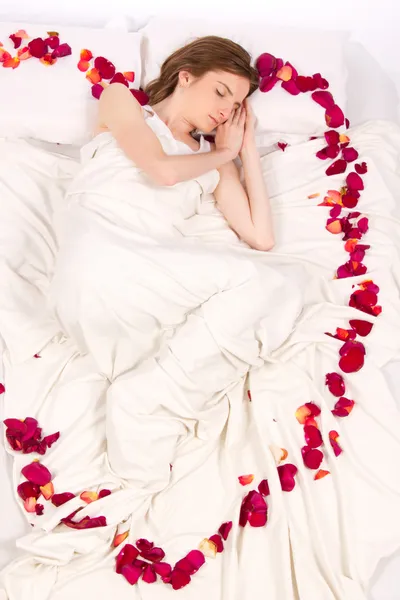 Donna attraente dormire a letto con petali di rose — Foto Stock