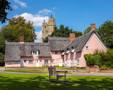 Suffolk, İngiltere - 11 Ağustos 2021: Bakire Meryem Kilisesi ve İngiltere 'nin Suffolk kentindeki Cavendish köyündeki pembe kulübelerin manzarası.