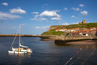 Whitby, İngiltere - 10 Haziran 2022: Kuzey Yorkshire, İngiltere 'deki Whitby sahil kasabasında çarpıcı Doğu Cliff ve Whitby Harbour manzarası. St. Mary Kilisesi uçurumun tepesine tünemiştir..