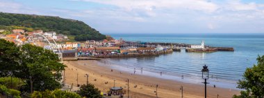 Scarborough, İngiltere - 8 Haziran 2022: Kuzey Yorkshire, İngiltere 'deki Scarborough sahil kasabasındaki büyük tekerlek, kale, iskele, deniz feneri ve plaj manzarası.