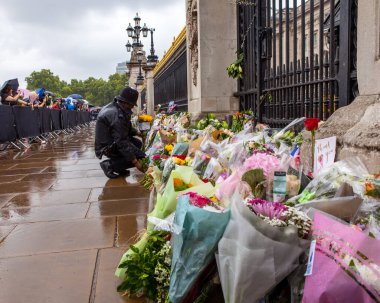 Londra, İngiltere - 9 Eylül 2022: Bir önceki gün ölen Kraliçe II. Elizabeth 'in anısına Londra' daki Buckingham Sarayı 'nın kapılarına çiçek bırakan bir polis memuru.