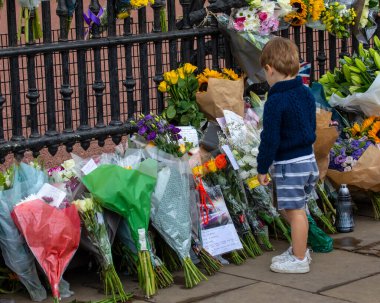 Londra, İngiltere - 9 Eylül 2022: Bir çocuk Londra 'daki Buckingham Sarayı' nda, bir önceki gün ölen II. Elizabeth 'in anısına bırakılan çiçeklere bakıyor..