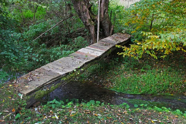 狭い小川を渡る古い木製の歩道橋 — ストック写真