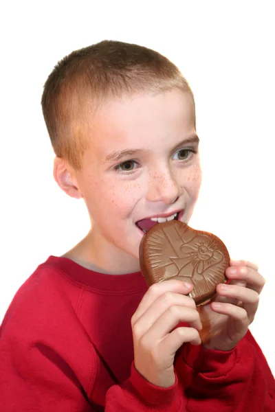 Menino feliz mordendo coração de chocolate — Fotografia de Stock