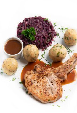 Alman usulü ızgara domuz pirzolası, ekmek köftesi ve beyaz arka planda geleneksel kırmızı lahana yemeği.