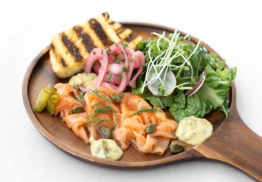 Beyaz arka planda salata ve tost kaplı somon gravlax tabağı.