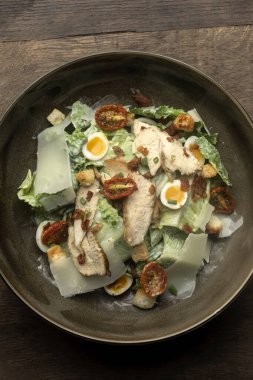 fresh chicken caesar salad in bowl on wood background