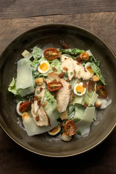 fresh chicken caesar salad in bowl on wood background