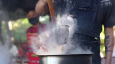 Sıcak erişte tenceresinin üzerinde paslanmaz çelik süzgeç. Akitchen 'de kaynayan buhardan beyaz duman çıkıyor. Tayland sokak yemekleri.