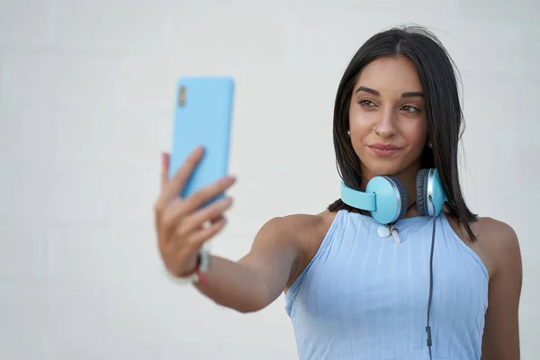 Belle femme prend un selfie avec le smartphone avec les écouteurs sur son cou — Photo