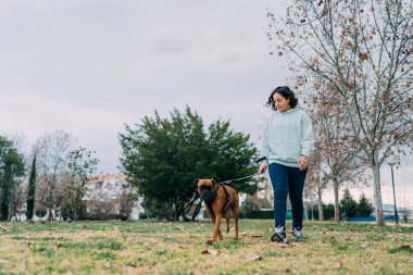 Kız, boksör köpeğiyle parkta yürüyor.