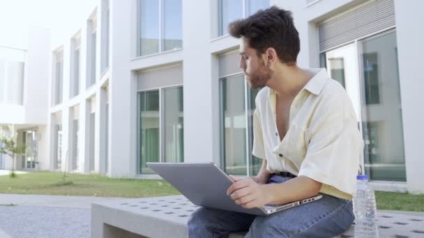 Jeune homme tapant sur son ordinateur portable assis sur un banc — Video