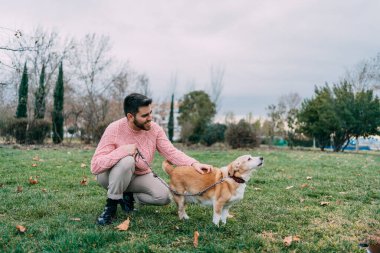Mutlu genç adam parkta köpeğini okşayarak çömeldi.