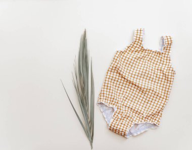 Bej arka planda palmiye yaprağı olan bebek mayosu, yaz tatili konsepti çok az. Düz yatış, üst görünüm