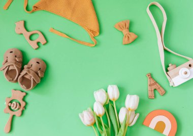 Yeşil arka planda bebek eşyaları ve aksesuarları. Tahta oyuncaklar ve düz laleler. Günlük arkaplanı