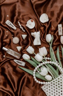 Beyaz laleler, inci çanta, parfüm şişesi, kadın aksesuarları ve kahverengi ipek arka planda bijouterie ile düz bir moda kompozisyonu. yaşam tarzı konsepti.