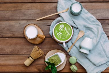 Beyaz bardakta yeşil kibrit çayı, çay tozu ve tahta kaşık. Sağlıklı bir içki. Üst manzara, düz uzanma.