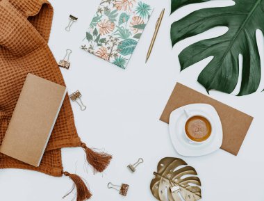 Üzerinde bilgisayar ve ofis malzemeleri olan beyaz bir çalışma masası. Boş defter, klavye, yeşil yaprak ve kahve fincanı olan düz bir çalışma masası. Reklam içeriğiniz için alanı kopyalayın