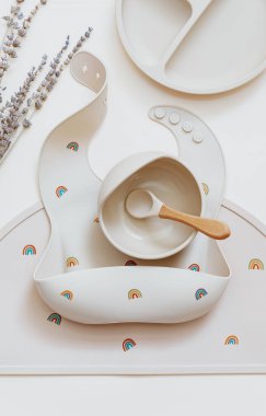 Bebek için silikon masa takımı, önlükler ve bej arka planda plaka içeren düz bir kompozisyon. Yemek servisi. Çocuk menüsü, beslenme ve beslenme kavramı