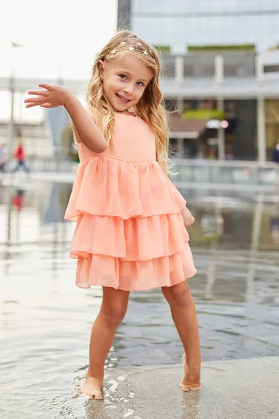 幸せな赤ちゃんの女の子は広場の噴水で水で遊ぶ — ストック写真