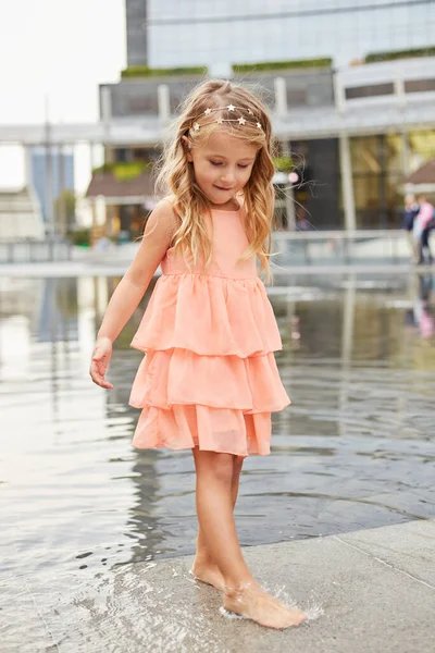 幸せな赤ちゃんの女の子は広場の噴水で水で遊ぶ — ストック写真