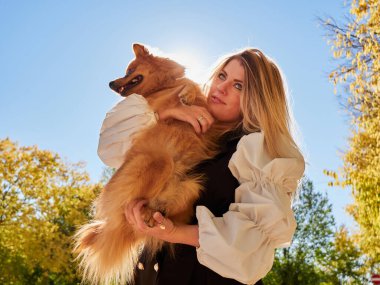 Güzel sarışın kız Pomeranya köpeğiyle oynuyor.