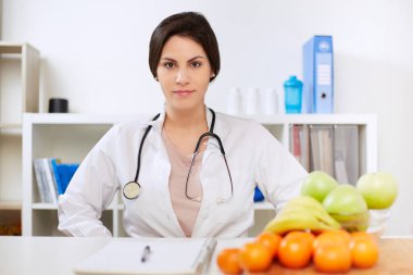 Güzel gülümseyen beslenme uzmanı kameraya bakıyor ve sağlıklı meyveler gösteriyor.