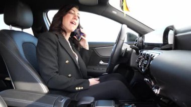 Güzel bir kadın arabanın içinde cep telefonuyla konuşuyor.