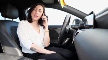 Güzel bir kadın arabanın içinde cep telefonuyla konuşuyor.