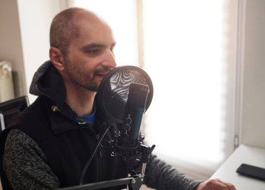 Yetişkin podcaster blogcusu, mikrofon kullanarak stüdyoda canlı yayın yaparken gülümsüyor.