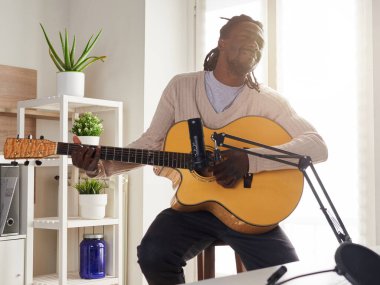 Genç adam evde ses kaydı yaparken şarkı söylüyor ve gitar çalıyor.