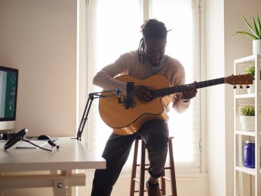 Genç adam evde ses kaydı yaparken şarkı söylüyor ve gitar çalıyor.
