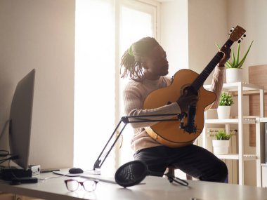 Genç adam evde ses kaydı yaparken şarkı söylüyor ve gitar çalıyor.