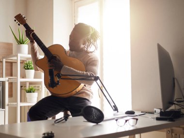 Genç adam evde ses kaydı yaparken şarkı söylüyor ve gitar çalıyor.