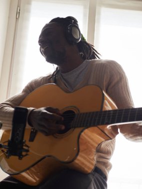 Genç adam evde ses kaydı yaparken şarkı söylüyor ve gitar çalıyor.