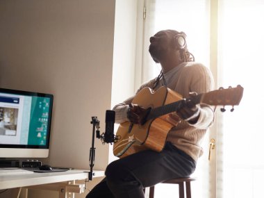 Genç adam evde ses kaydı yaparken şarkı söylüyor ve gitar çalıyor.