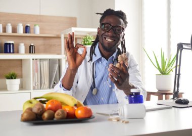 Afroamerikan beslenme uzmanı kameraya bakıyor ve danışmada zencefil gösteriyor.