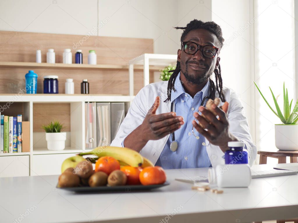 Afroamerican nutritionist looking at camera and showing ginger in the consultation.