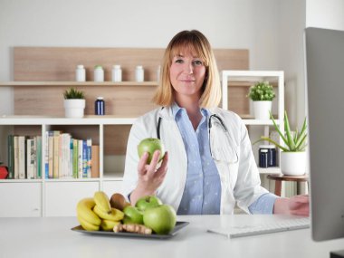 Stüdyoda elinde yeşil elma tutan kadın beslenme uzmanı.