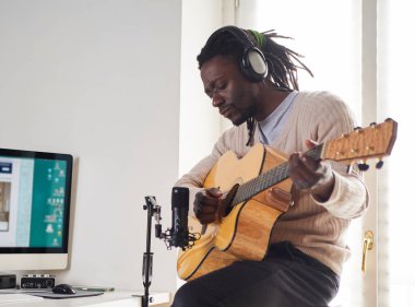 Genç adam evde ses kaydı yaparken şarkı söylüyor ve gitar çalıyor.