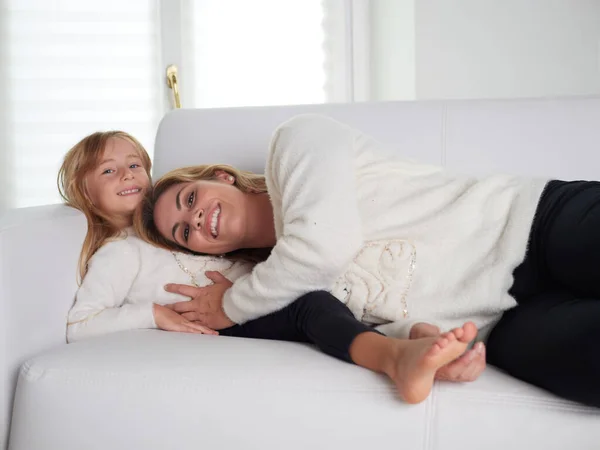 年轻的母亲和女儿躺在白色的沙发上 — 图库照片