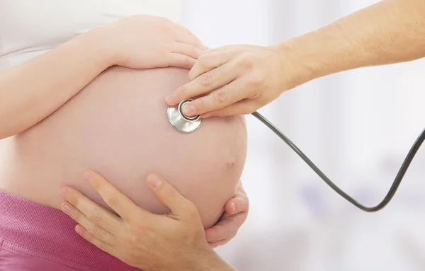 Belly of pregnant woman and hand of doctor with a stethoscope — Stock Photo, Image