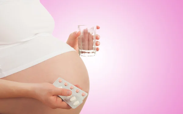 Belly of pregnant woman and vitamin pills and glass of water — Stock Photo, Image