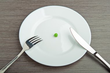 Diet concept. one pea on an empty white plate clipart