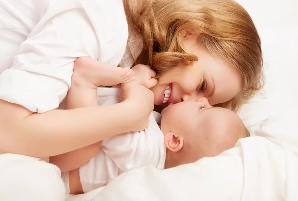 Gelukkige familie. baby en moeder spelen, kiss, kietelen, lachen in bed — Stockfoto