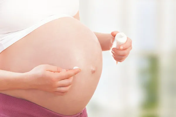 Buik van zwangere vrouw en hydraterende crème — Stockfoto