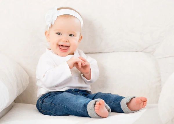 Happy little baby girl laughing and sitting on a sofa in jeans — Stock Photo, Image