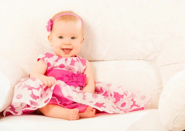 Hermosa niña en un vestido rosa sentado en el sofá en casa — Foto de Stock